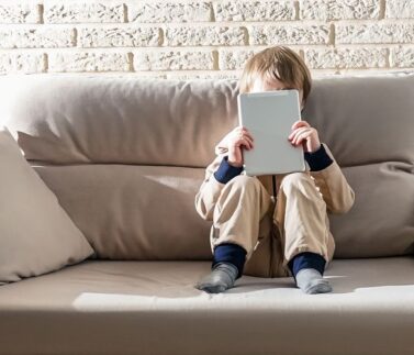 Kid in casual clothes on sofa use laptop. Lockdown concept, technology.
